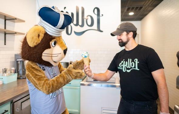 A man hands ice cream to a lion mascot.